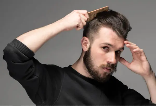 Man med skägg och mustasch kammar sitt hår som har en snygg taper fade.